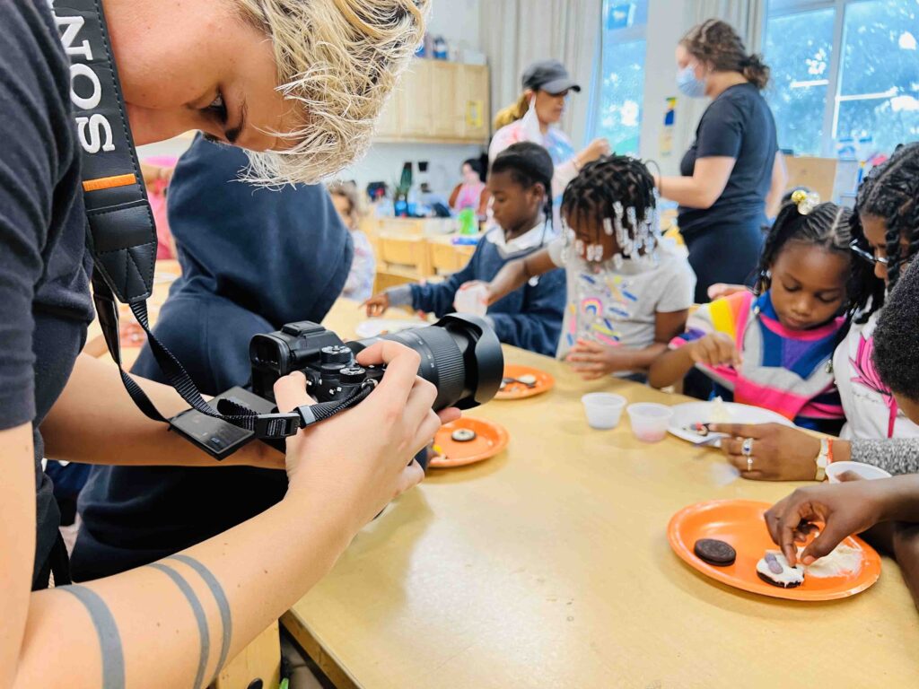 A filmmaker filing young girls eating snacks at a long table.