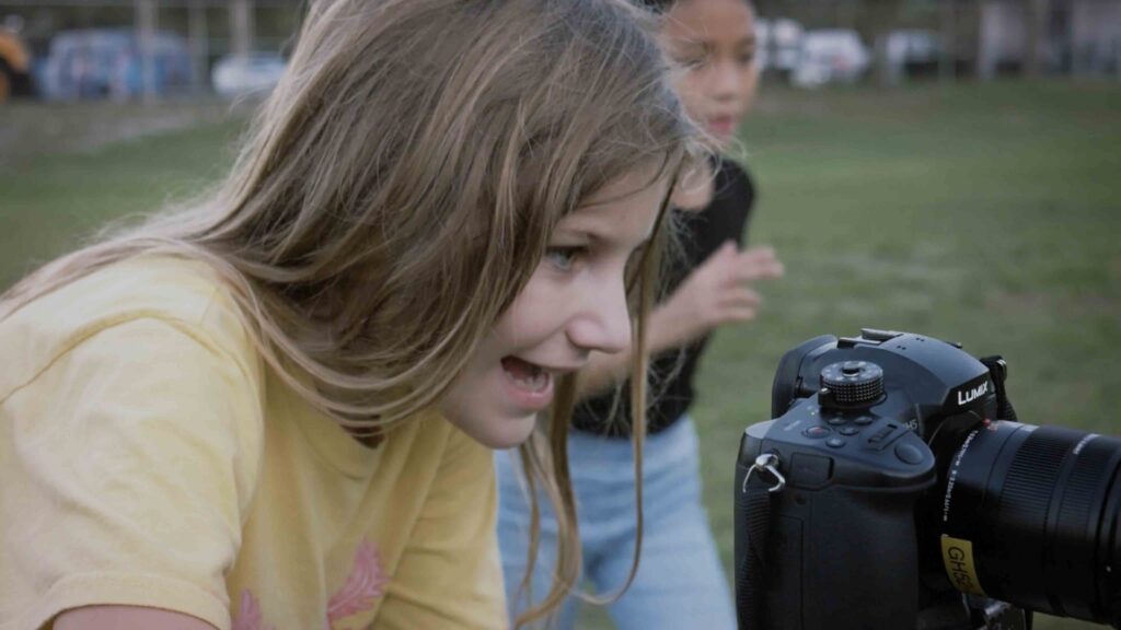 Young girl looking through the viewfinder of a high-end video production camera being used to film a charity video.
