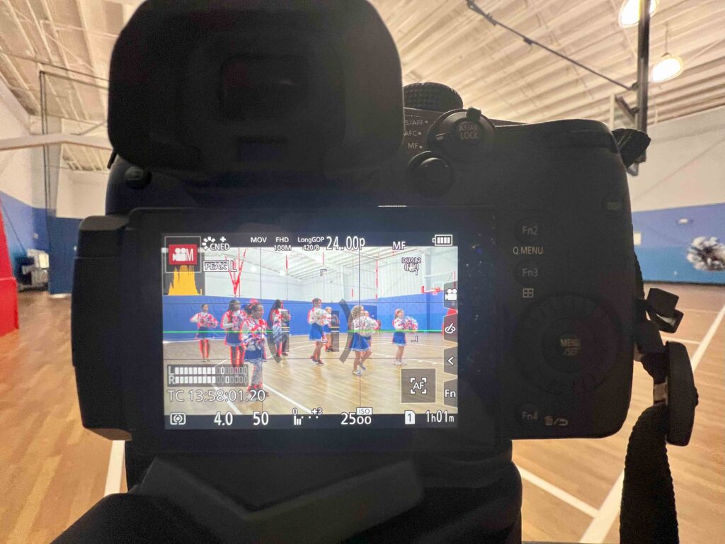 Heads-up display of a camera filming a non profit video for the boys and girls club showing young cheerleaders on a basketball court.